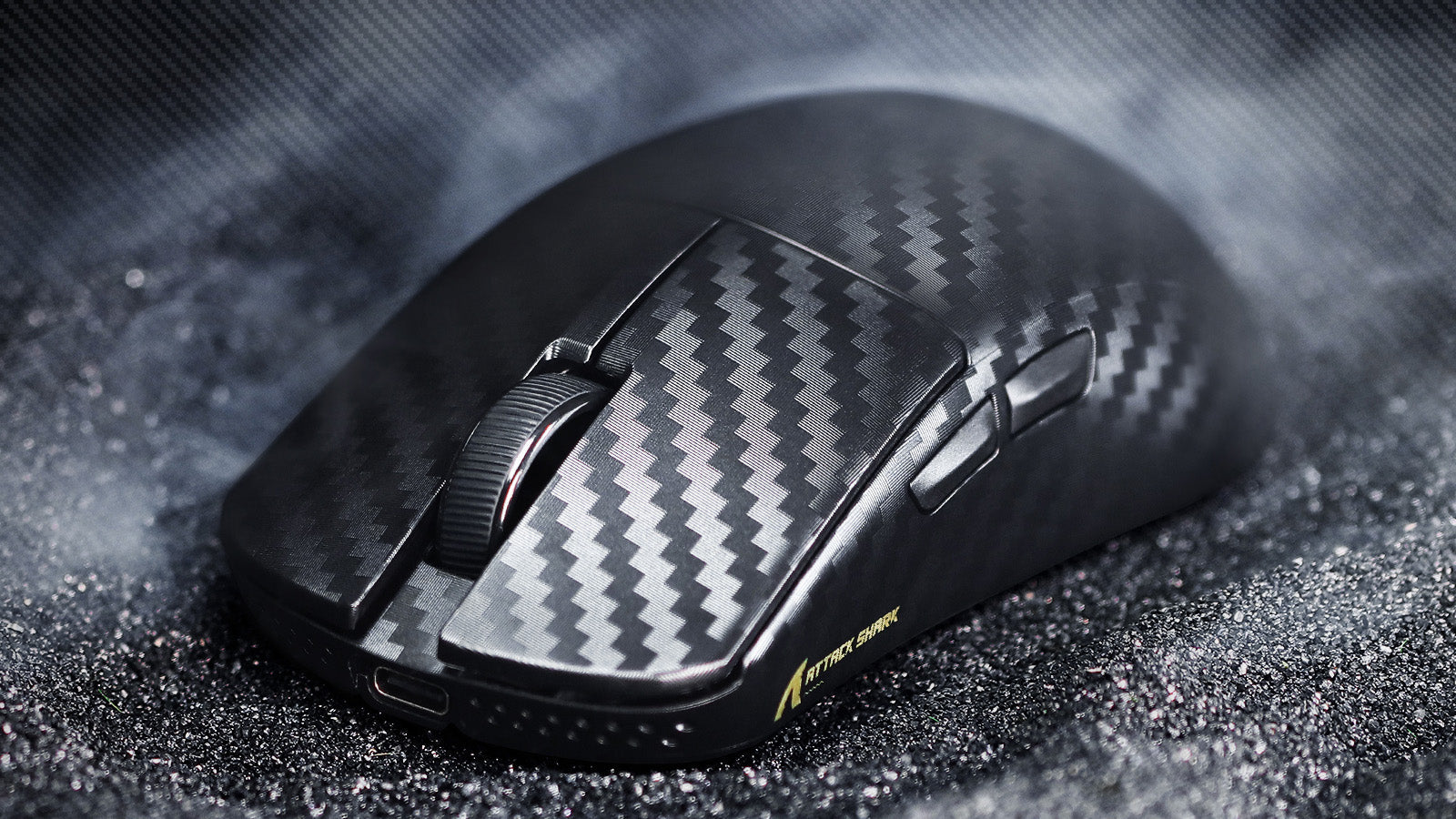 Black gaming mouse with carbon fiber pattern texture, featuring side buttons and a ribbed scroll wheel, displayed on a dark sparkly surface
